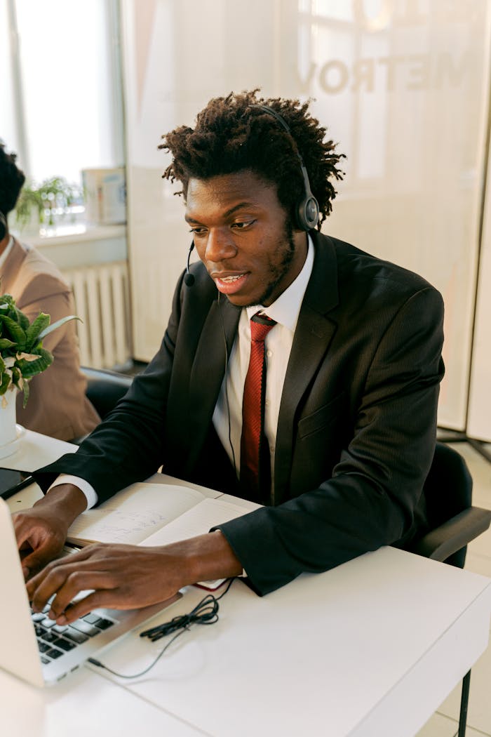 African American man in a suit using a laptop and headset for customer support.
